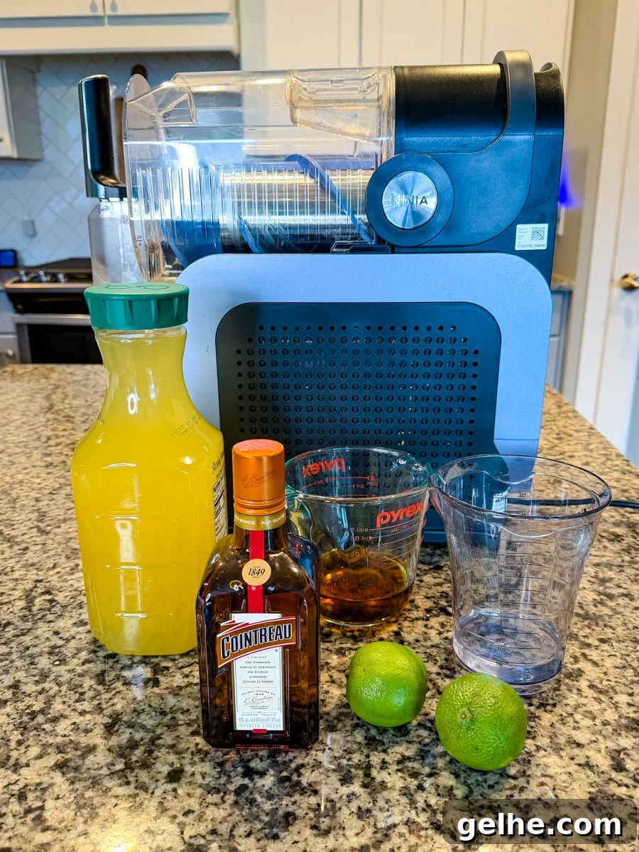 A countertop setup with the Ninja Slushi machine and ingredients arranged in front: a bottle of juice, a bottle of Cointreau, a measuring cup of dark rum, an empty cup, and two whole limes.