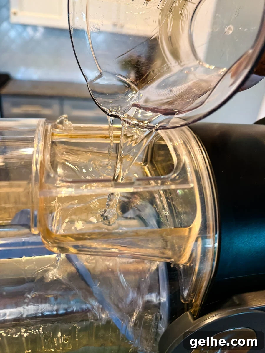 A clear measuring cup pouring a transparent liquid into the Ninja Slushi machine as the drink mixture begins to freeze inside.