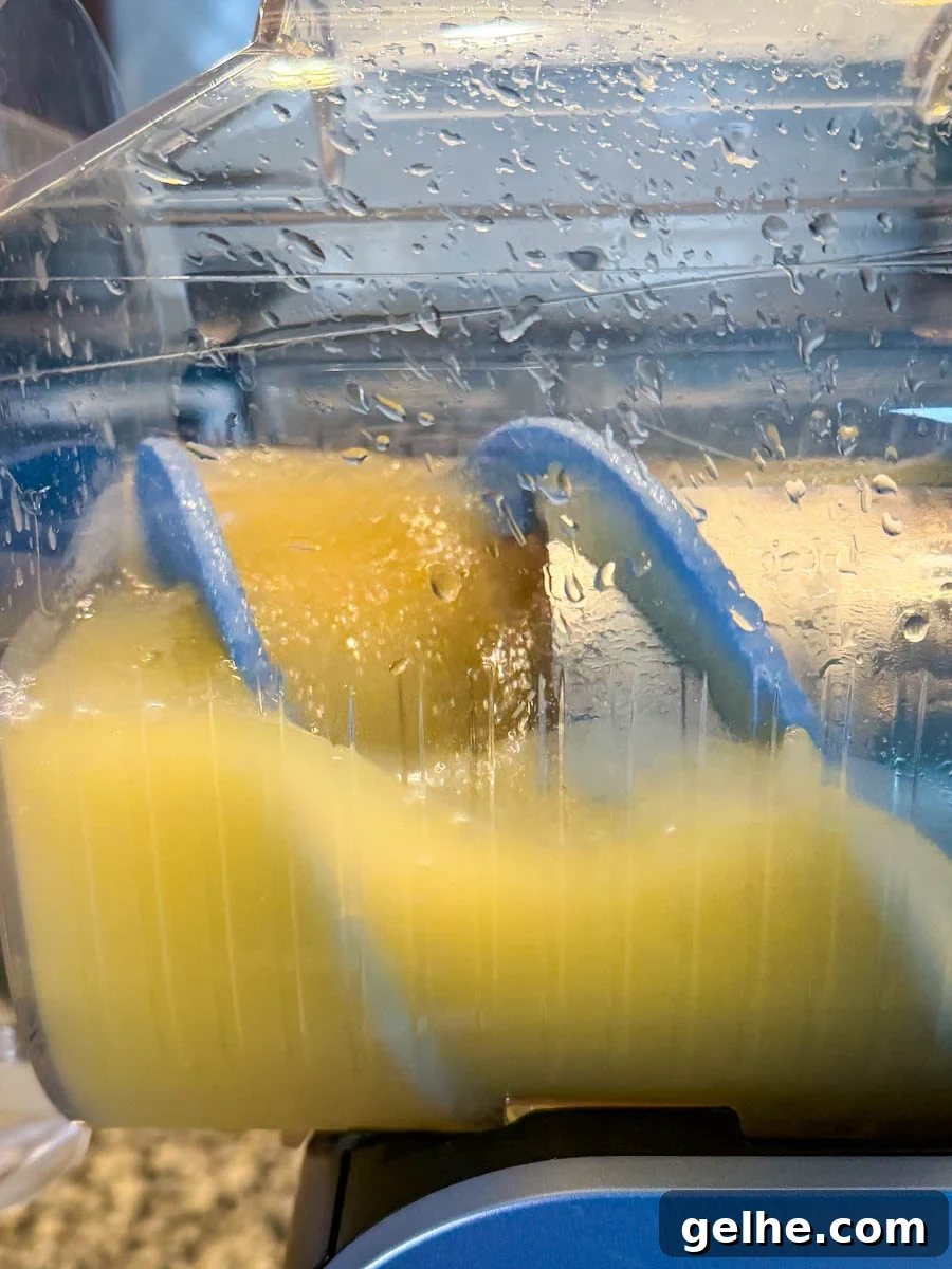 Mai Tai mixture further along in the freezing process inside the Ninja Slushi machine, with the rotating paddle moving through the icy orange slush.
