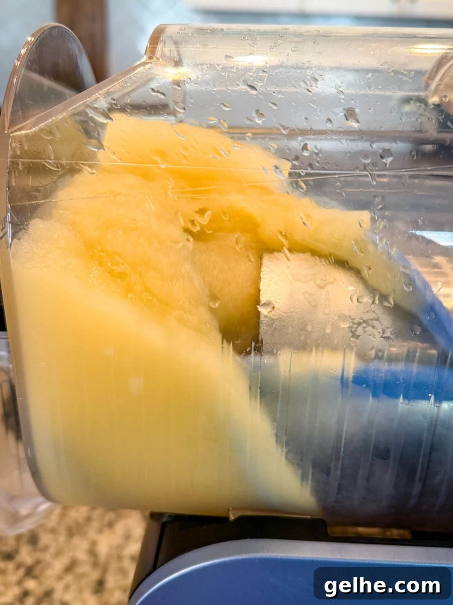 Close-up view inside the Ninja Slushi machine showing the Mai Tai mixture beginning to freeze into a thick, pale orange slush.