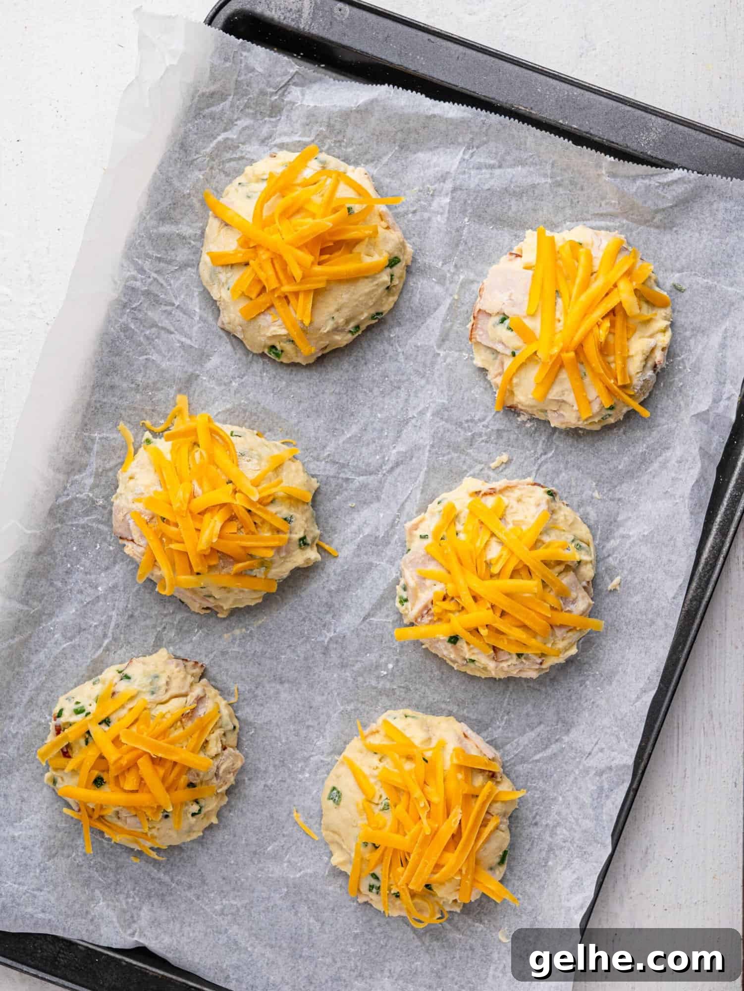 High-Protein Biscuits Without Butter – Fluffy, Low-Fat Recipe 14 Protein biscuits topped with cheese on a baking tray before baking.