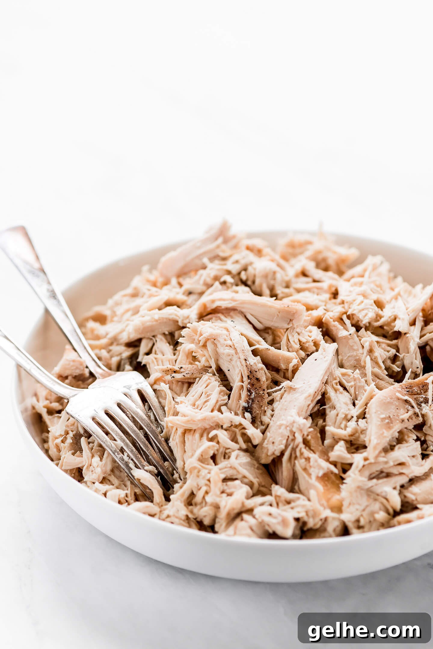 Slow Cooker Shredded Chicken in a large white serving bowl with two forks in the side. 