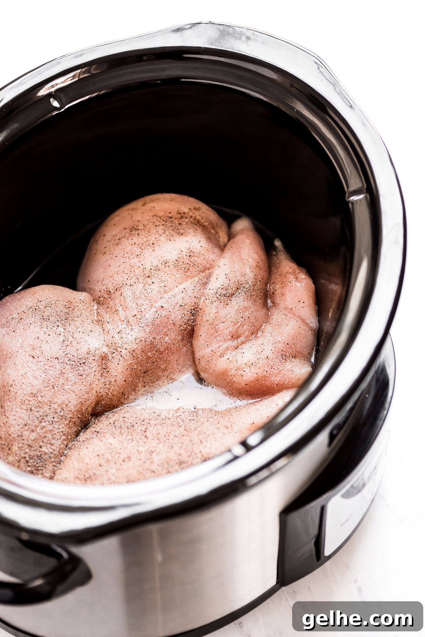 Raw boneless skinless chicken breasts in the bottom of a slow cooker seasoned with spices.