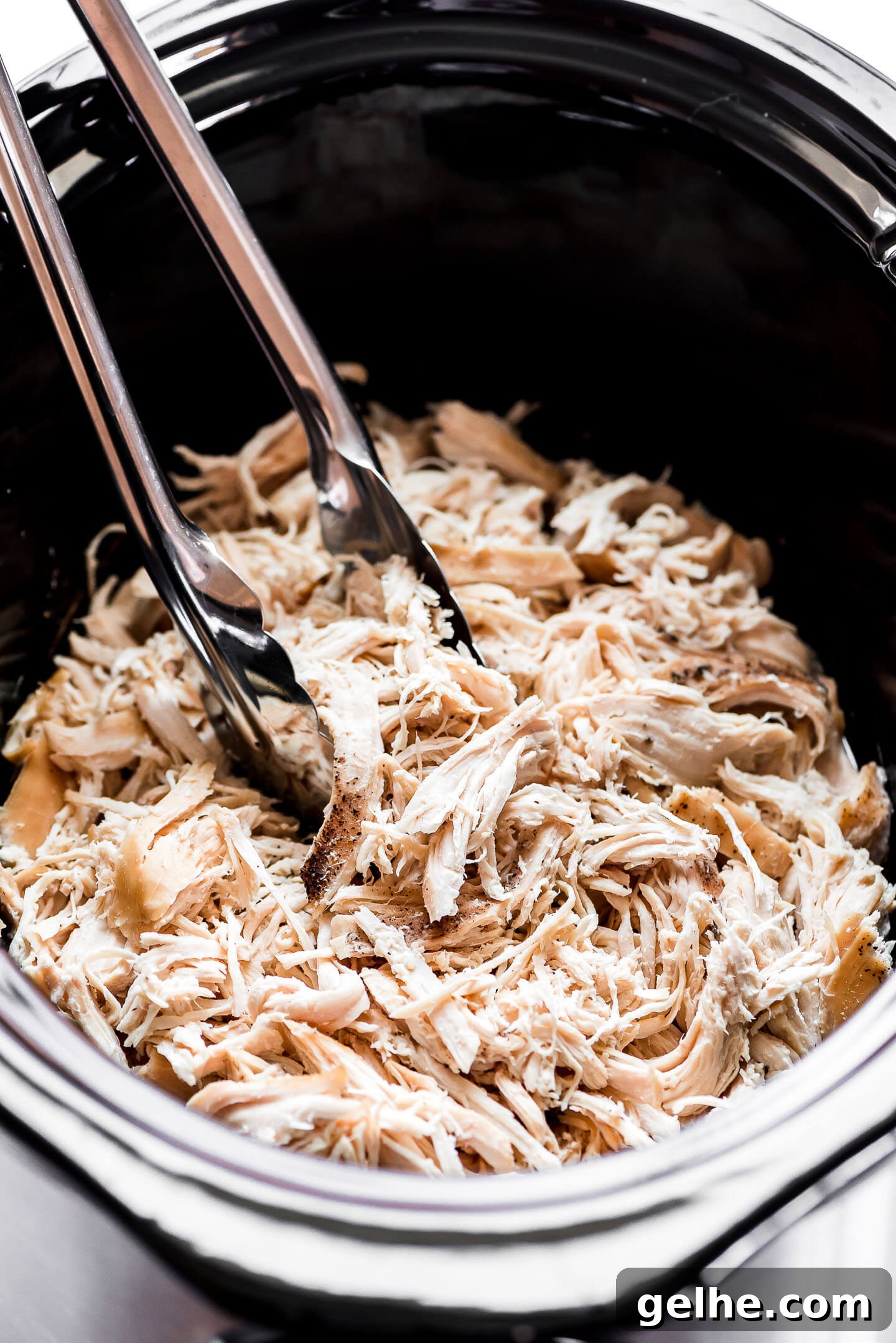 Shredded chicken in a Crock-Pot with tongs about to lift some out.