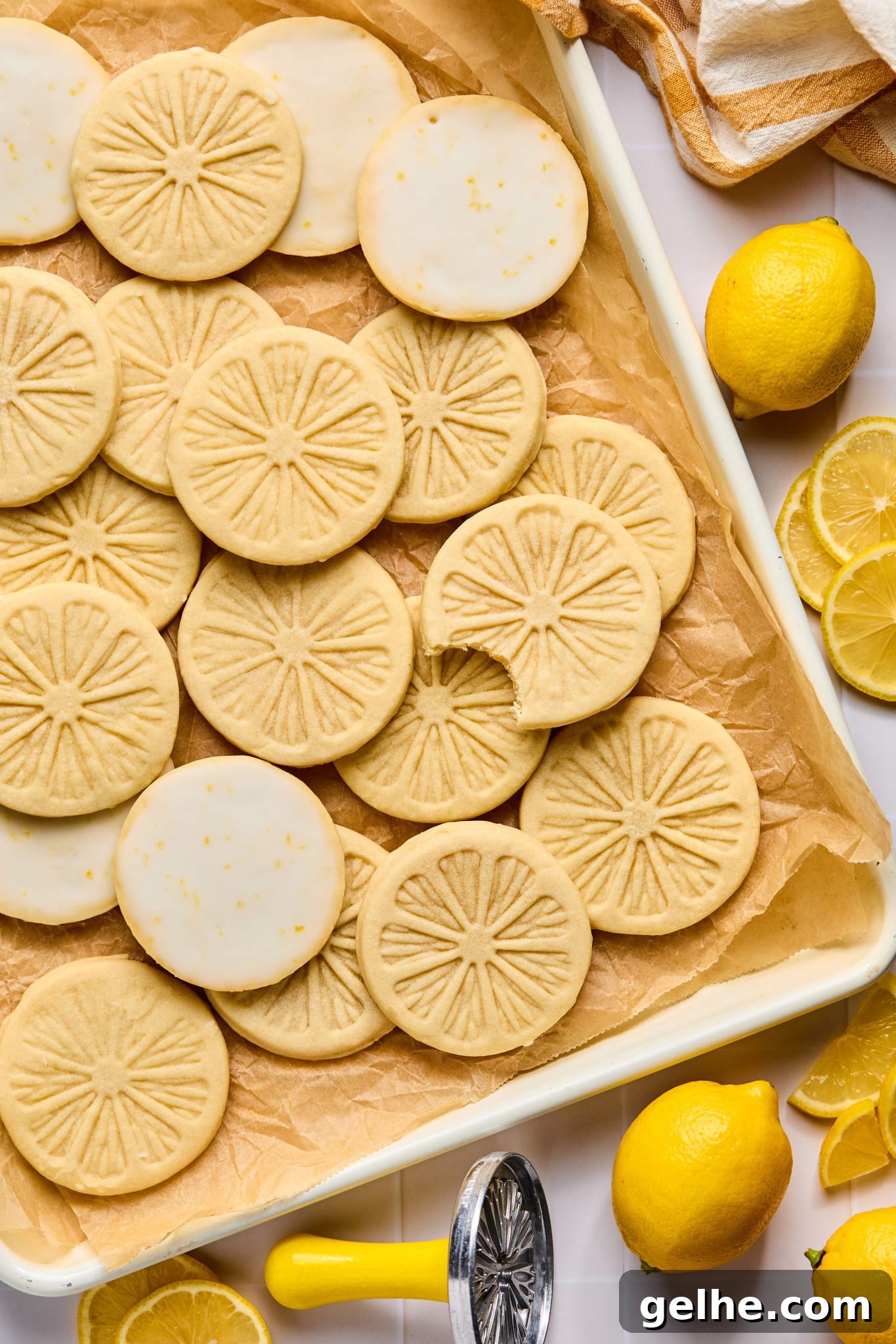 Homemade Girl Scout Lemonade Recipe: Refreshing Copycat Version 12 Picture of lemonade cookies on parchment-lined baking sheet. One cookie has a bite taken out of it. There are lemons and the metal lemon stamp surrounding the baking sheet.