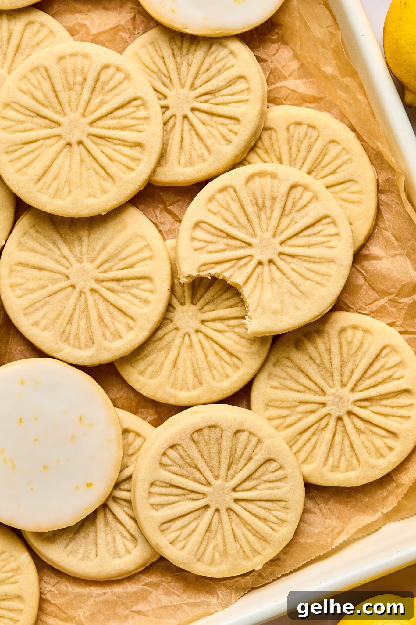 Homemade Girl Scout Lemonade Recipe: Refreshing Copycat Version 6 Lemonade cookies on parchment-lined baking sheet after they have finished setting from being dunked in the glaze. One cookie has a bite taken out of it and two of the cookies are showing the lemon glaze on the bottom.