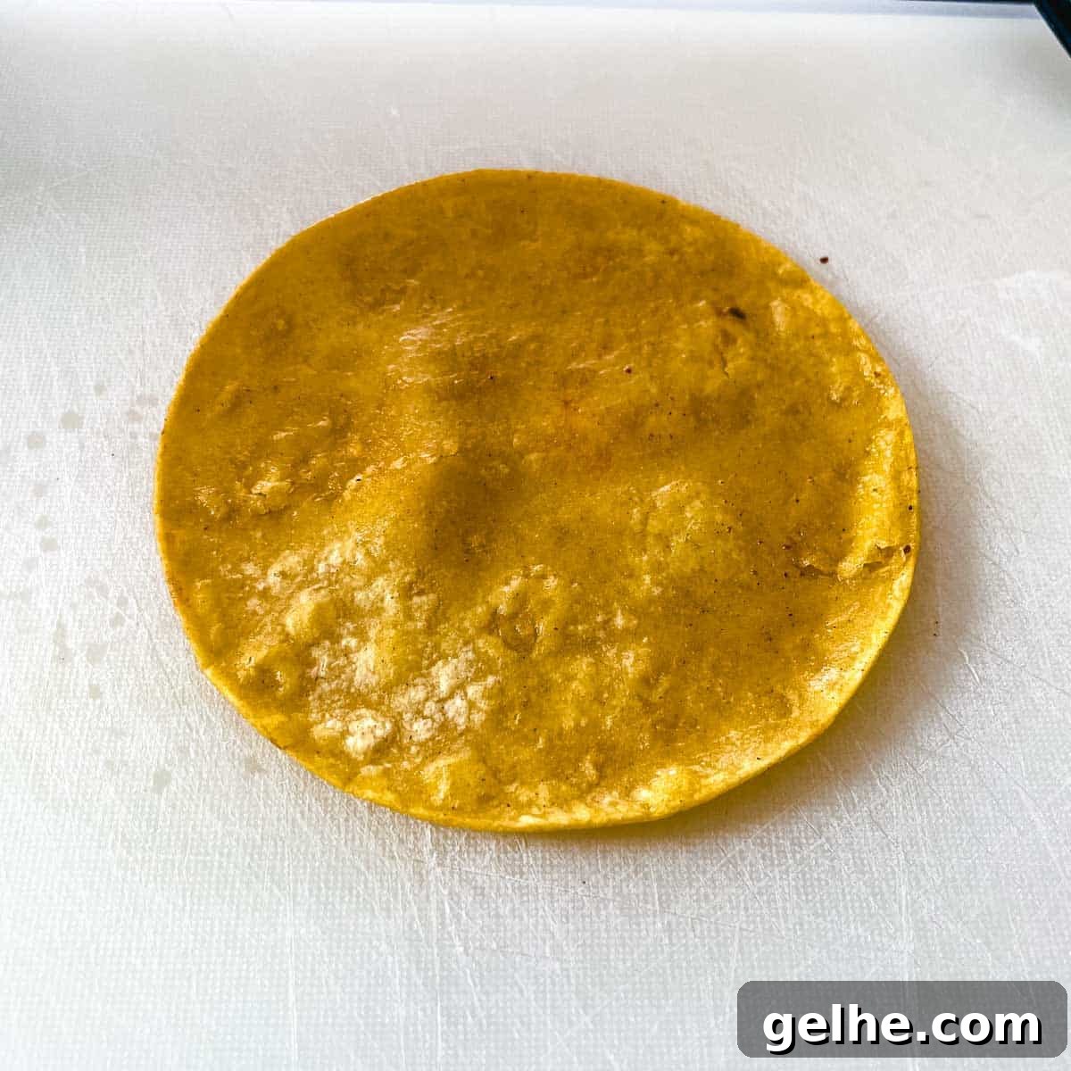 Slow Cooker Shredded Chicken Enchiladas Recipe 9 A fried corn tortilla sits on a white cutting board.