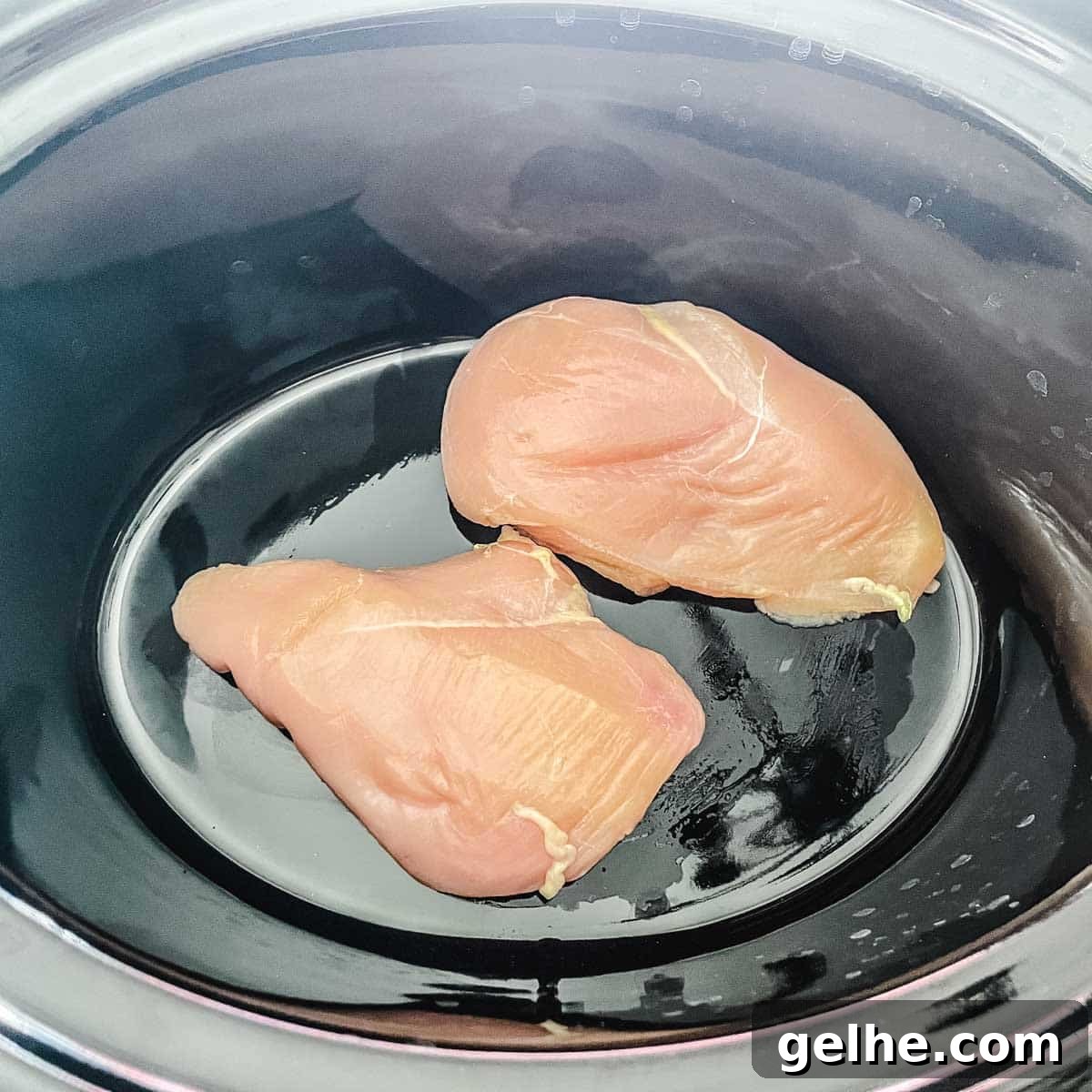 Slow Cooker Shredded Chicken Enchiladas Recipe 5 Two chicken breasts are placed in the base of a slow cooker.
