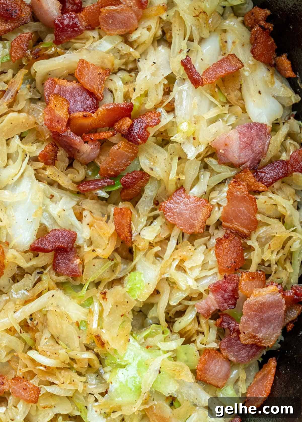 a cast iron skillet full of fried cabbage and crispy bacon with tender onions