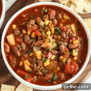 Cowboy soup with ground beef, beans, veggies, herbs in a bowl; saltine crackers on the side.