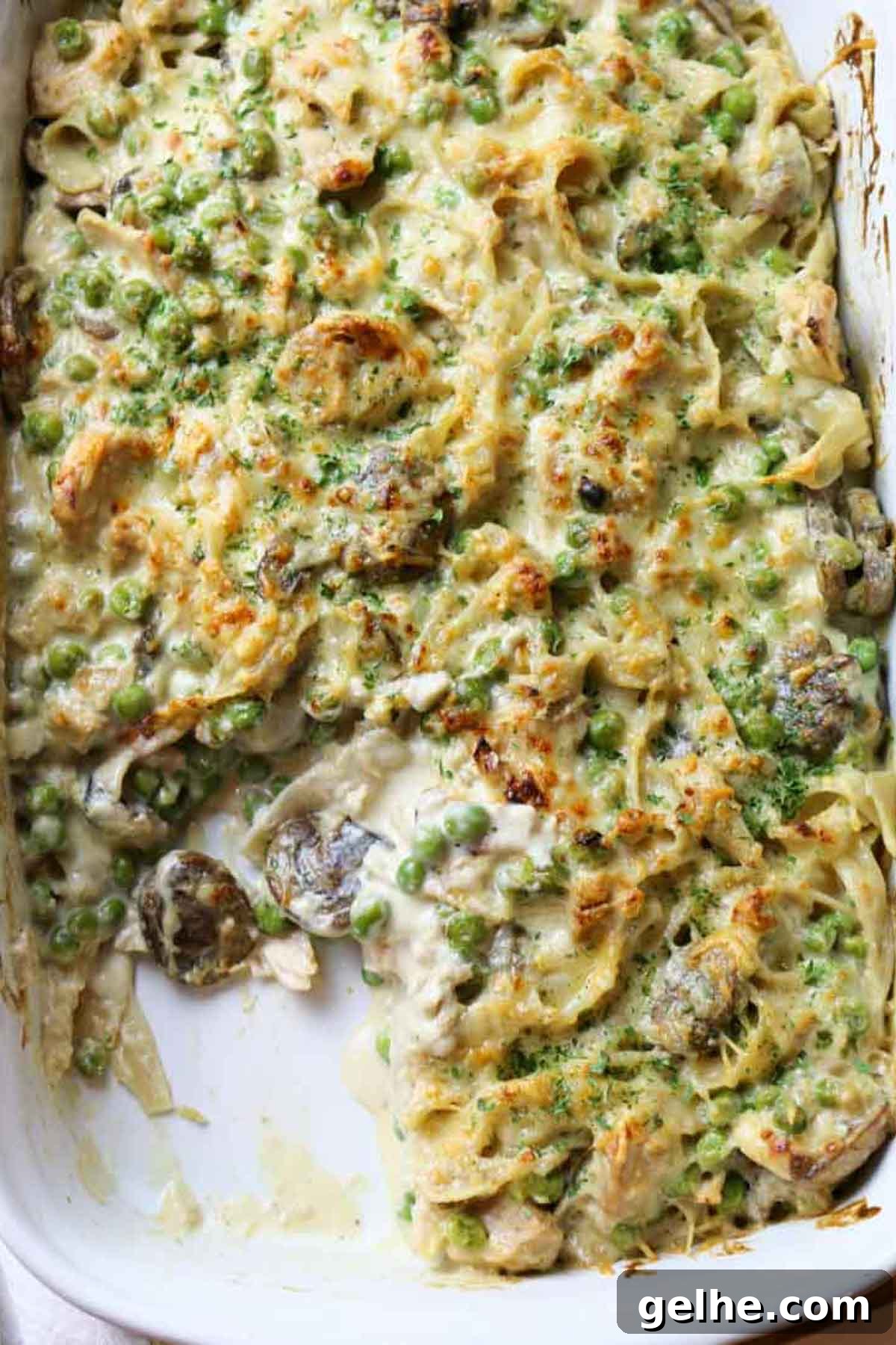 tuna noodle casserole with mushrooms and peas in white dish.