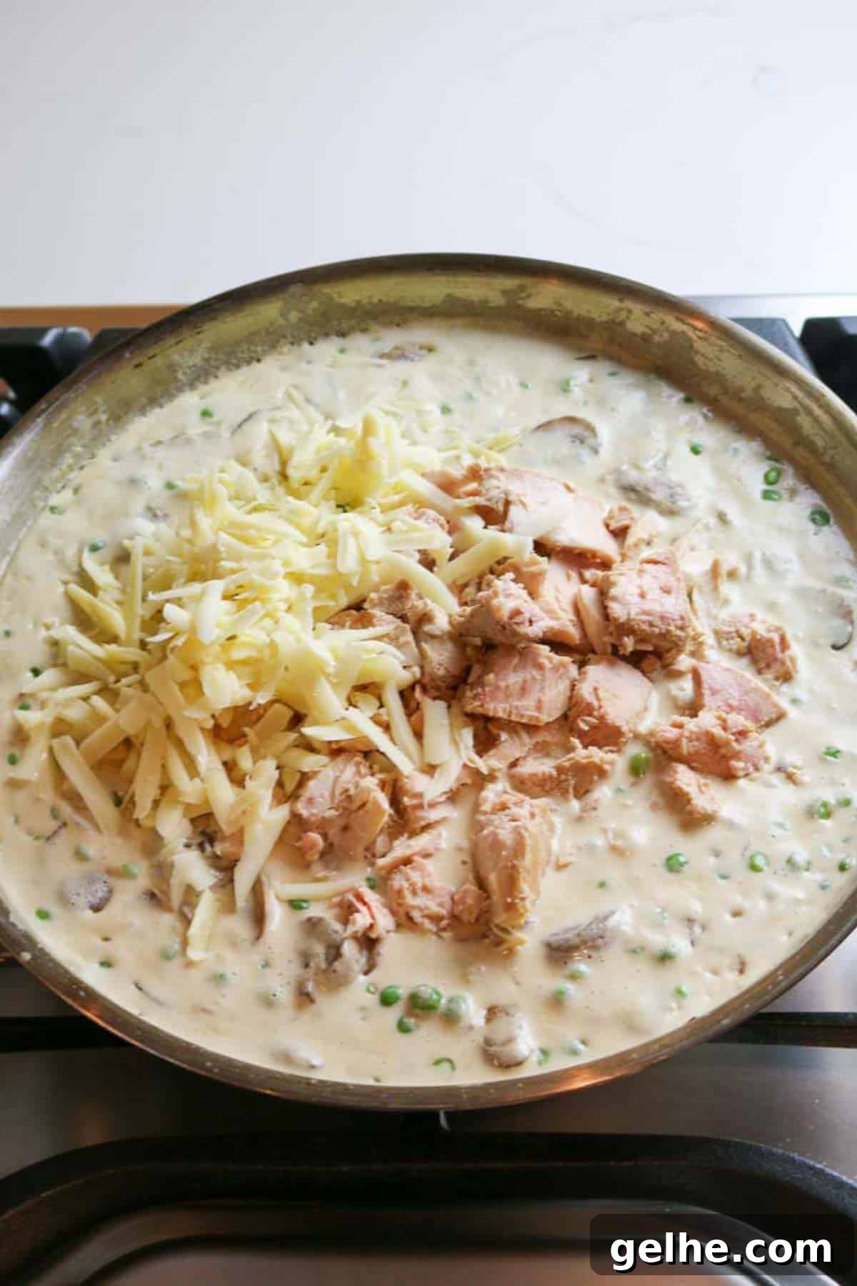 flaky tuna with cheese added to creamy mixture in skillet.