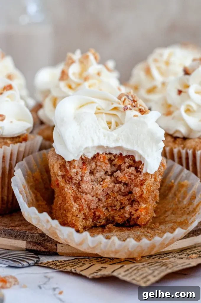 An orange gluten-free carrot cake cupcake topped with white cream cheese frosting and chopped nuts. The cupcake liner is pulled down and there is a large bite taken out of the cupcake.