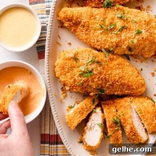 hand dipping slice of panko baked chicken into dipping sauce with platter of chicken on the side