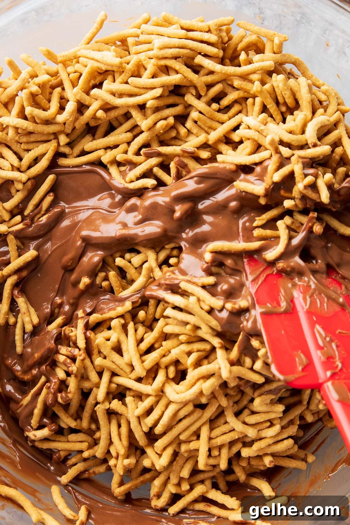 Folding melted chocolate and butterscotch mixture with chow mien noodles in mixing bowl.
