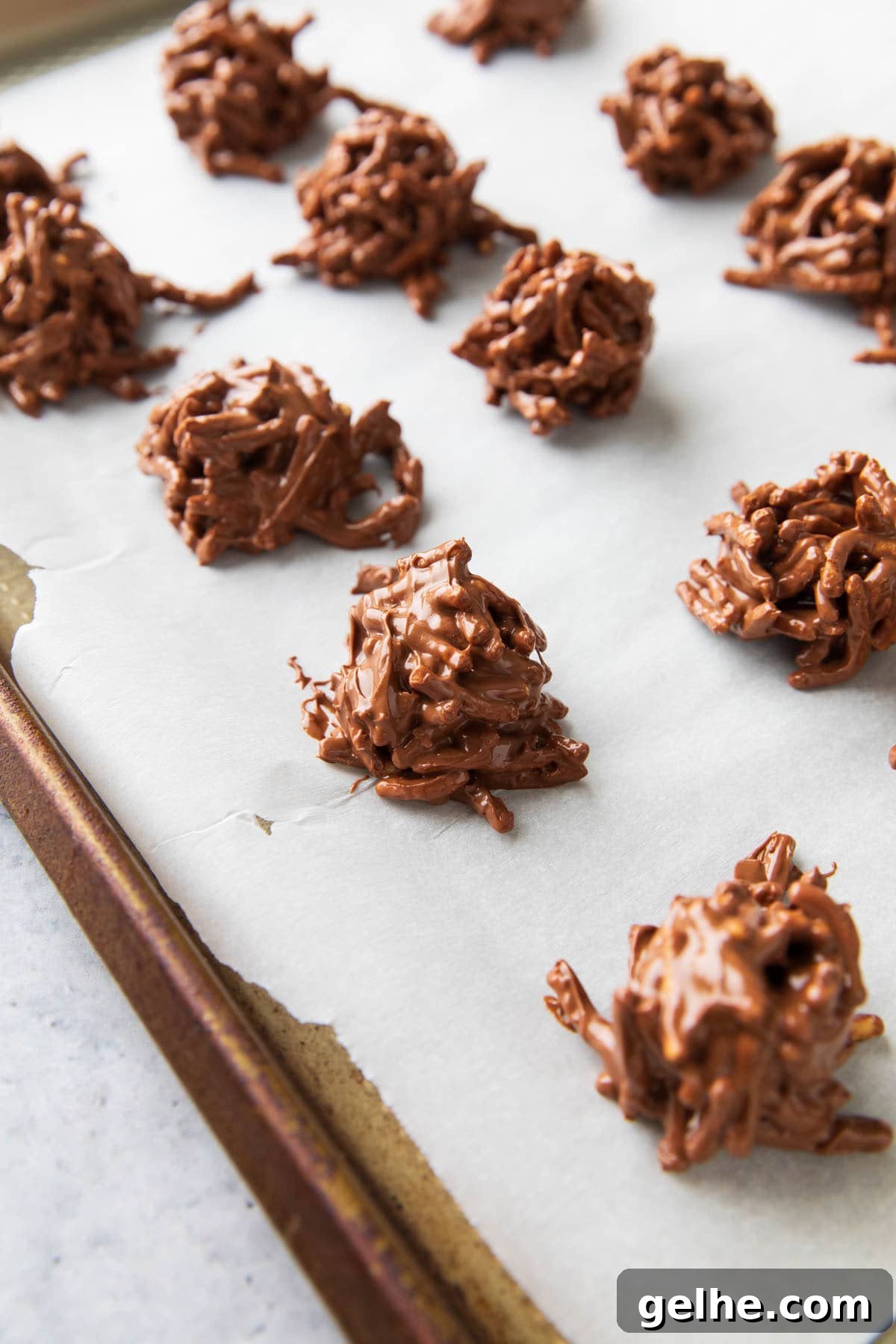 Lines of haystack cookies - Neatly scooped no bake Christmas cookies on a parchment lined baking sheet.