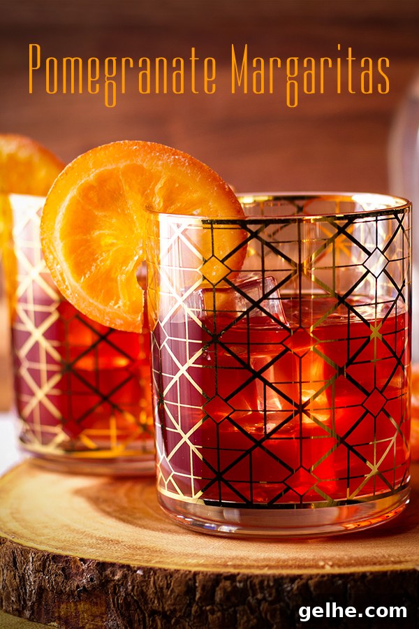 Two pomegranate margarita cocktails garnished with orange slices.