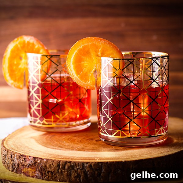 Two glasses on a wood serving board filled with ice and pomegranate margaritas and garnished with orange slices.