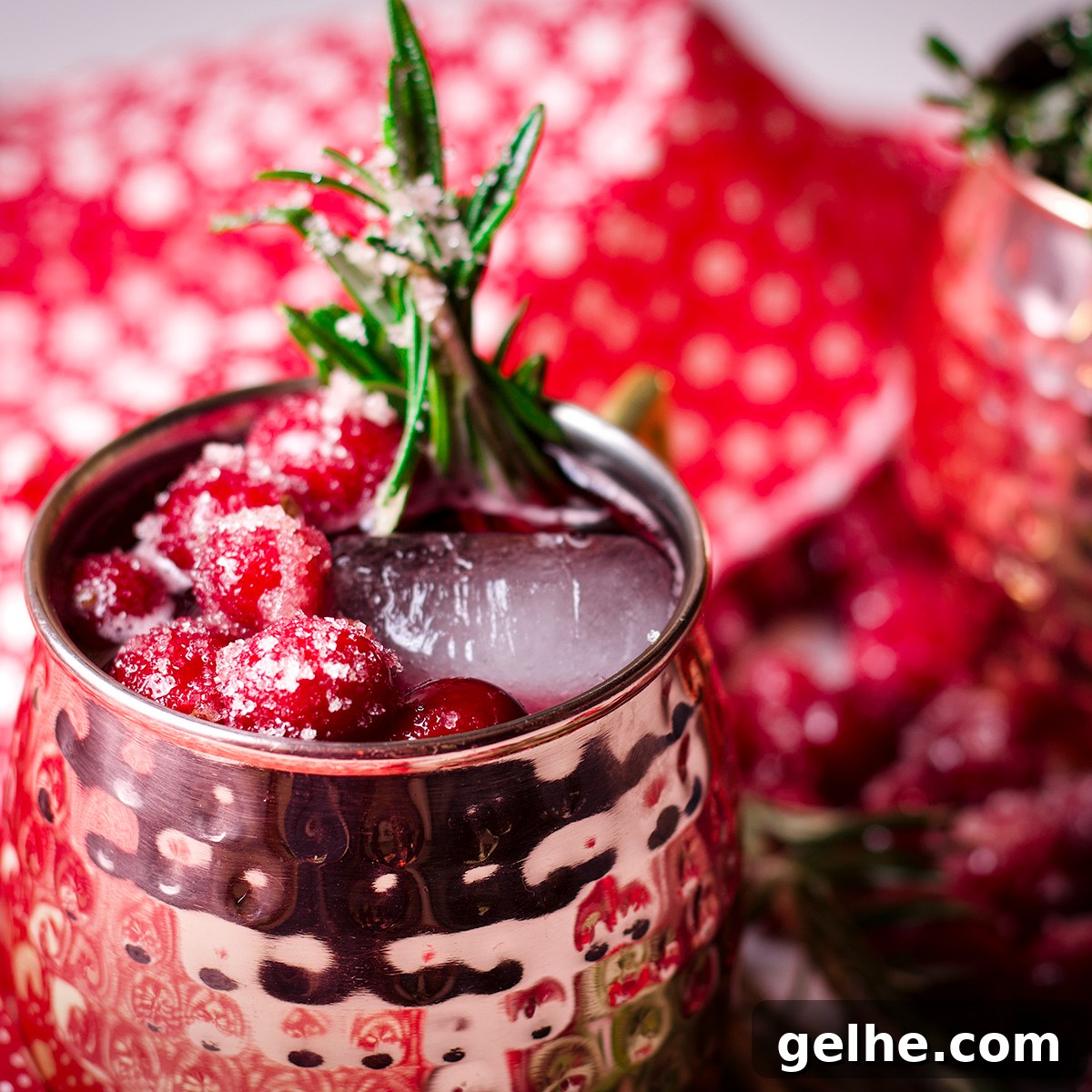 Two Cranberry Moscow Mule cocktails in copper mugs garnished with sugared cranberries and fresh rosemary.