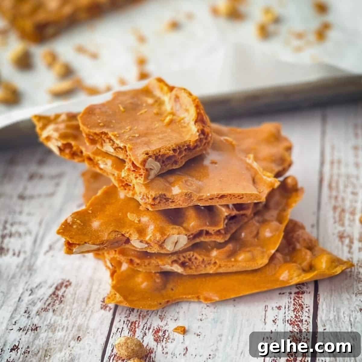 Soft peanut brittle stacked on top of each other with a pan of the rest of the brittle in the background.