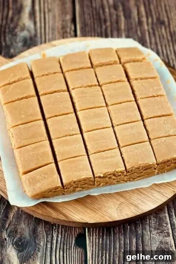 Creamy peanut butter fudge cut into small squares on a round cutting board.