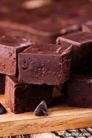 Small pieces of two ingredient chocolate fudge stacked on a wooden cutting board.