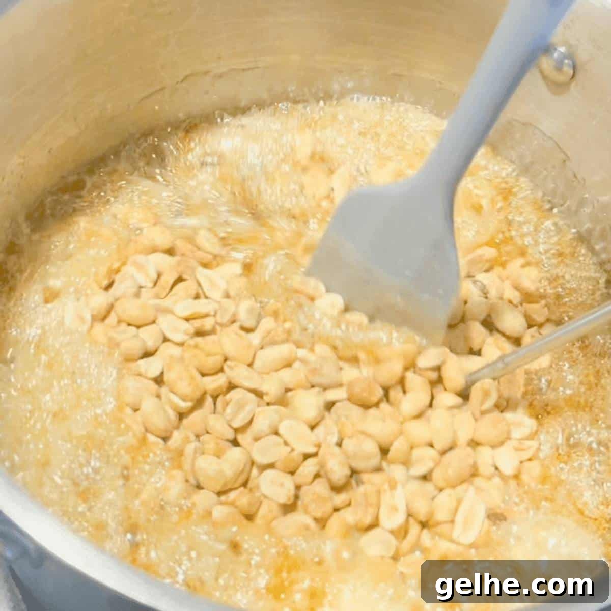 A spatula stirring in the butter and peanuts in a large pot.