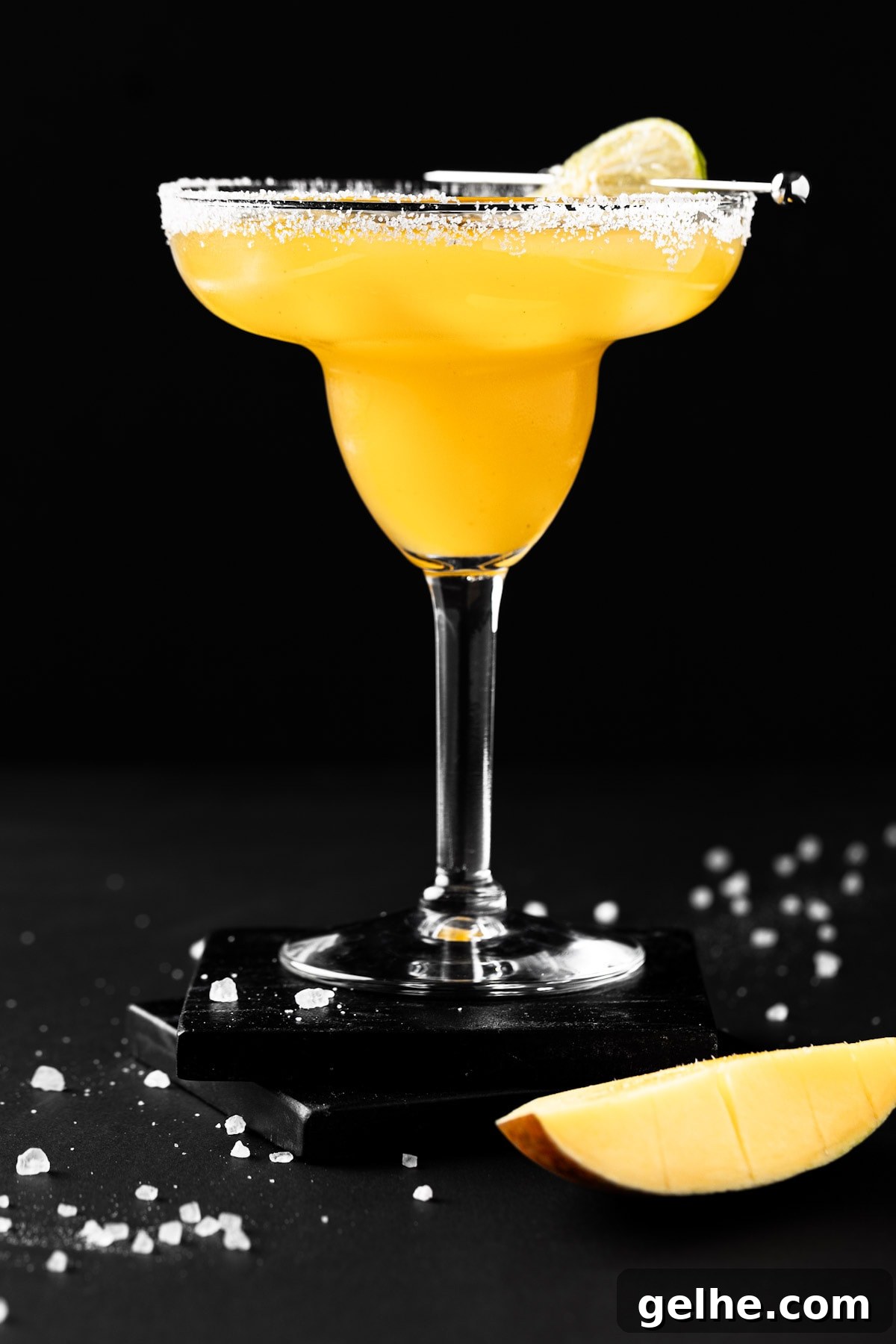 A mango margarita on the rocks with a salted rim, on a black background.