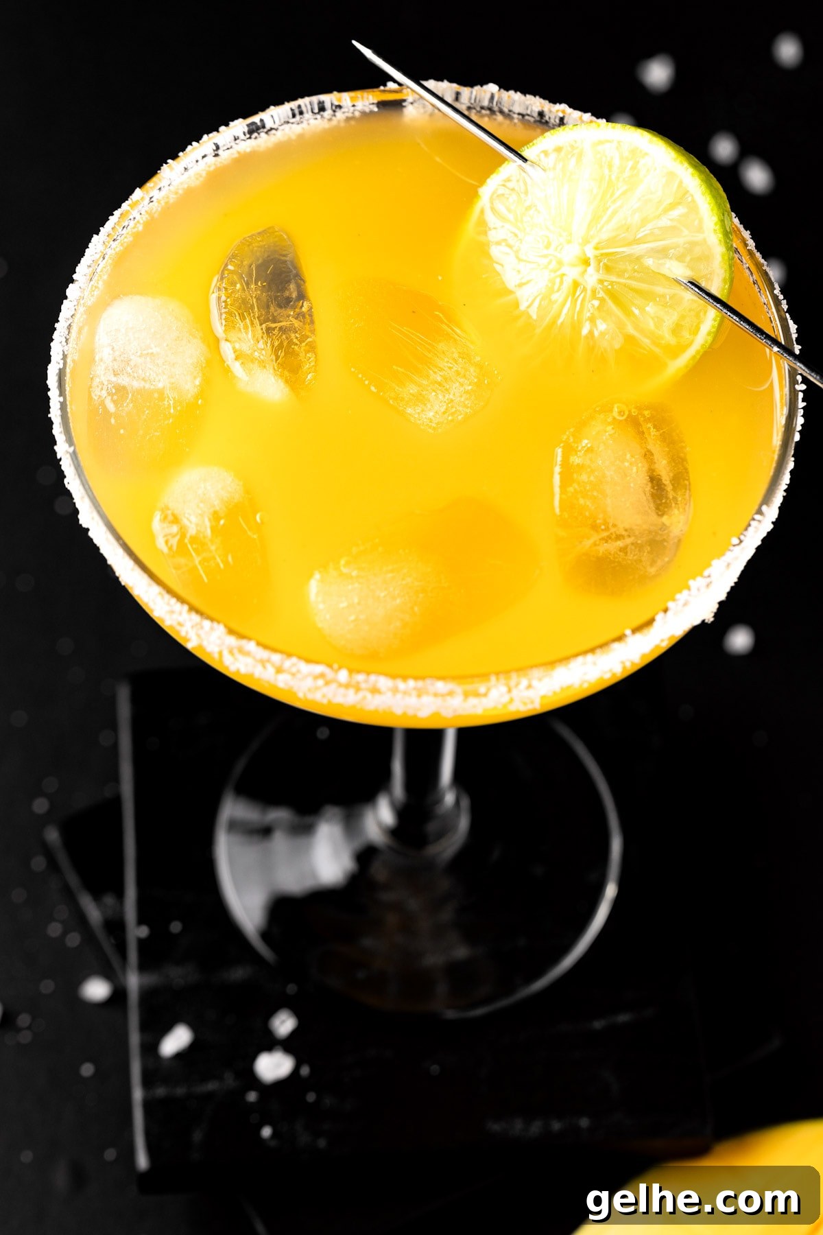 Overhead view of a mango margarita on the rocks, garnished with lime on a black table.