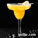 A mango margarita on the rocks with a salted rim, on a black background.