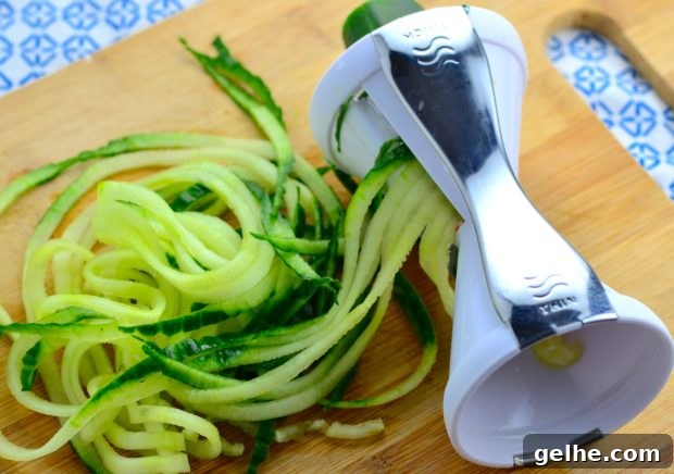 Spiralized zucchini noodles coming out of a manual vegetable spiralizer