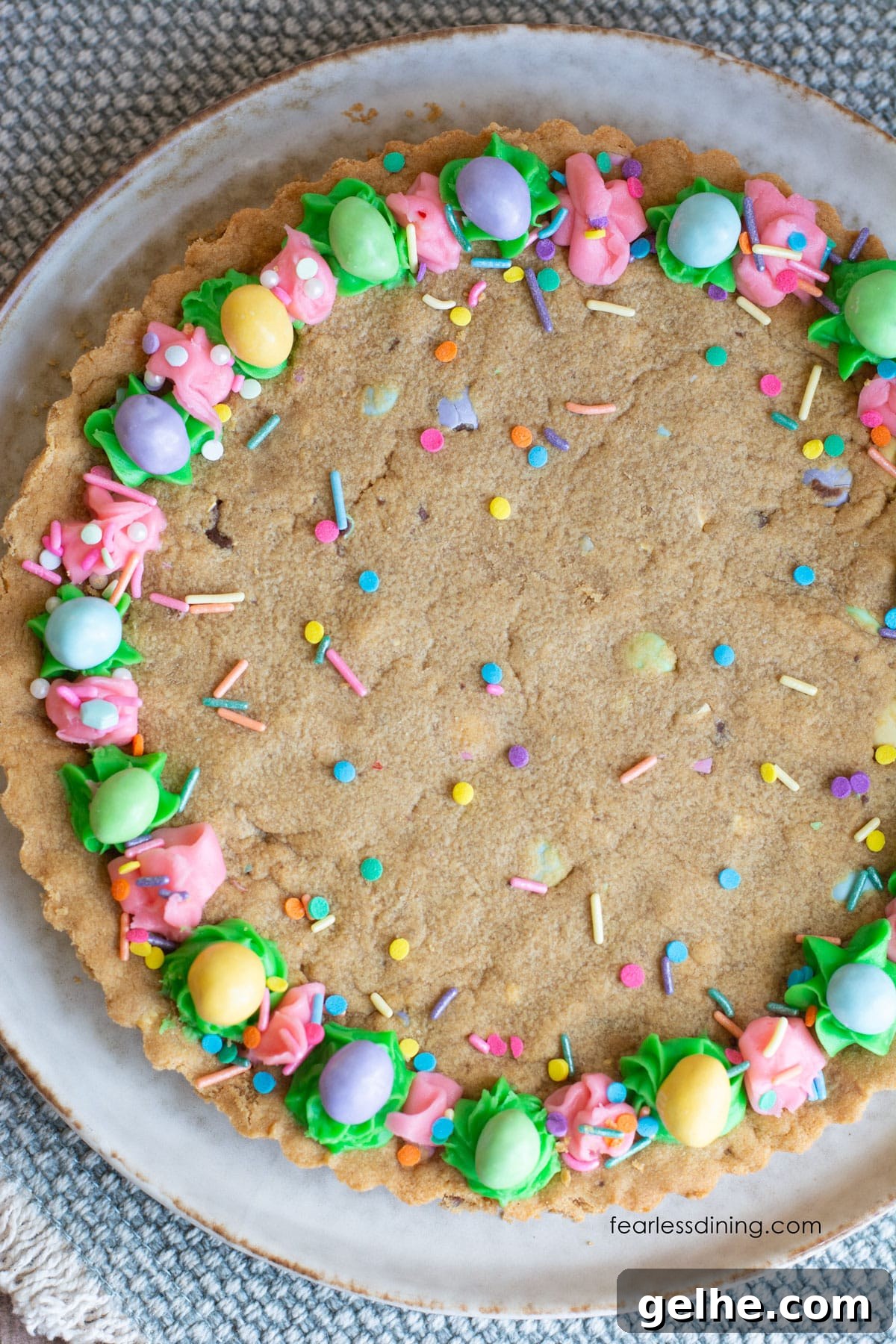 Gluten-Free Peanut Butter Cookie Cake Recipe for Dense, Chewy Slices 2 The top view of a gluten free peanut butter cookie cake. It is loaded with M and Ms and decorated with pastel frosting and sprinkles.