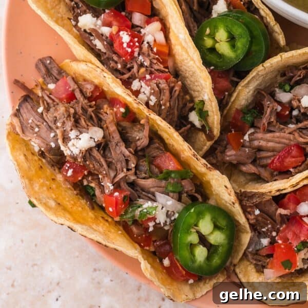 Crispy Homemade Crunchwrap Recipe: Copycat Taco Bell Wrap 16 A plate of four shredded beef tacos topped with diced tomatoes, onions, jalapeños, and crumbled cheese.