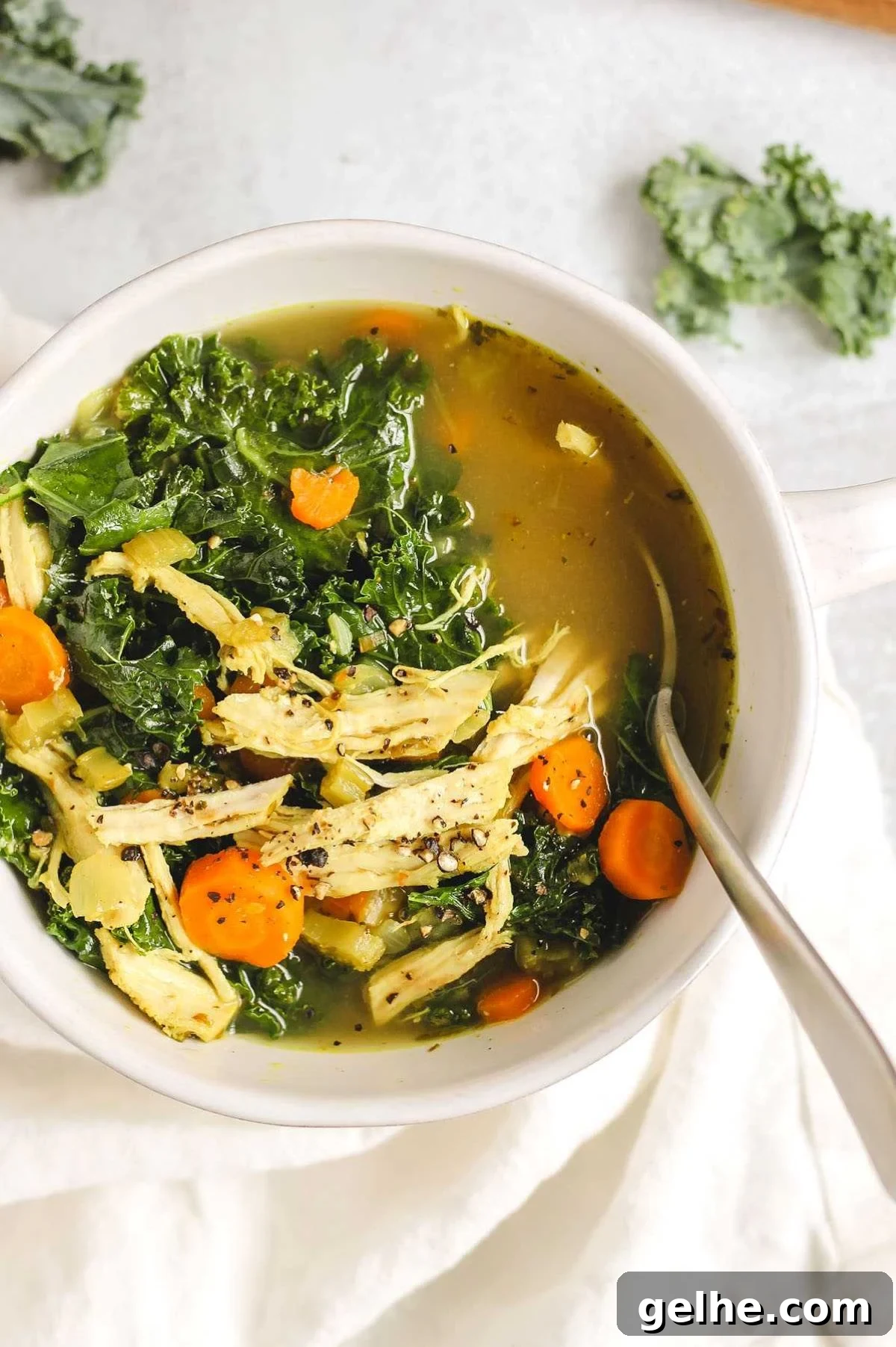 Chicken and kale soup in a white soup bowl with a spoon.