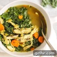 Chicken and kale soup in a white soup bowl with a spoon.