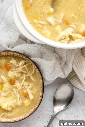 A bowl and larger soup crock next to each other filled with creamy chicken and cauliflower soup.