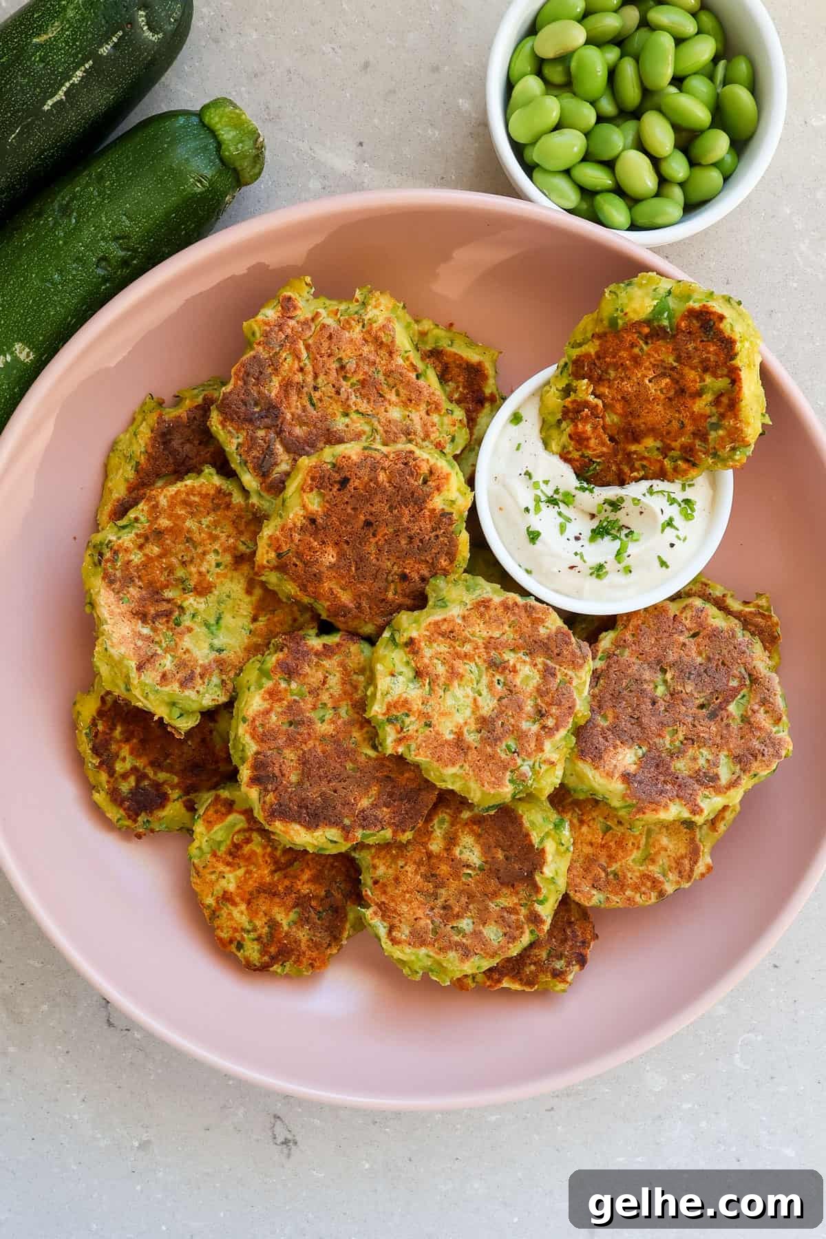 Zucchini and edamame fritters dipped in yoghurt sauce.