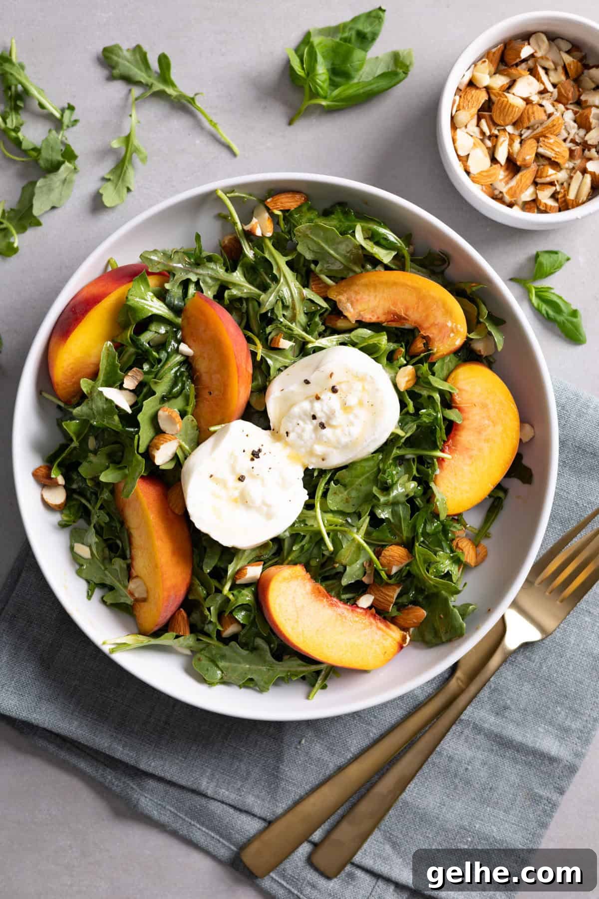 A bowl of arugula burrata salad with peaches and almonds.