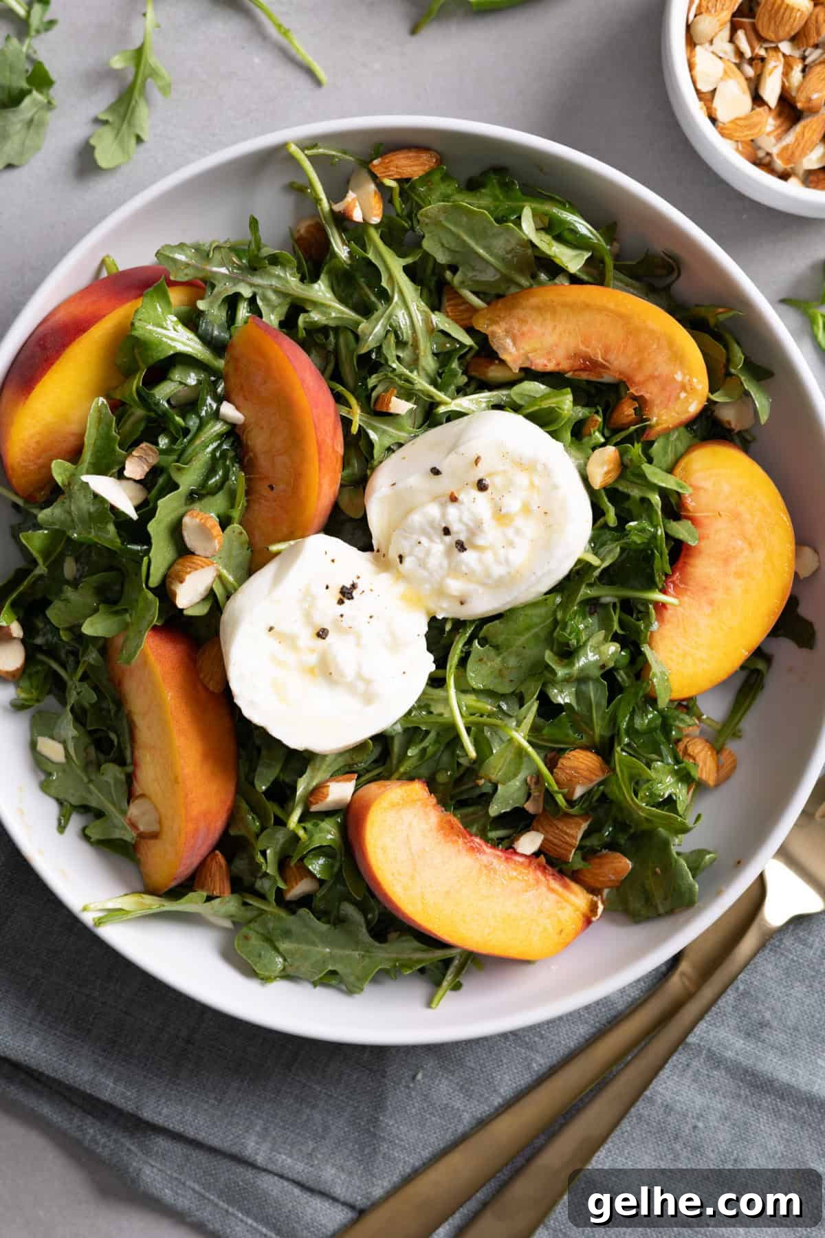 Close up of a serving of arugula burrata salad with peaches and almonds.