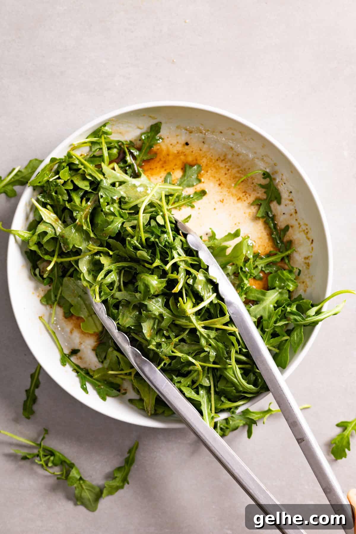 Arugula getting tossed in a bowl with balsamic vinaigrette.
