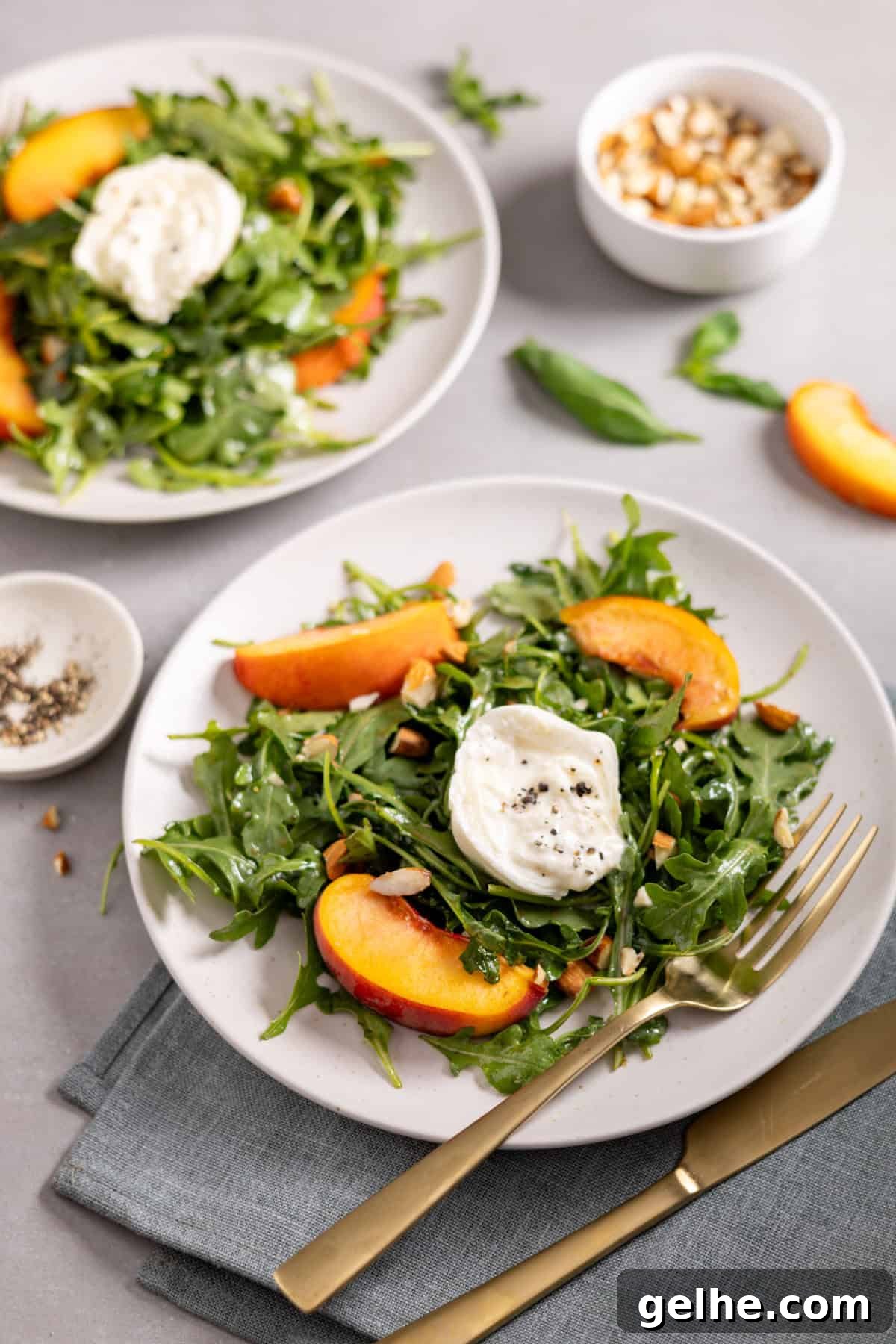 Two plates of arugula burrata salad topped with peaches and almonds.