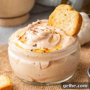 Square close up of pink-orange thick sauce in a glass jar with toasted bread stuck in it.