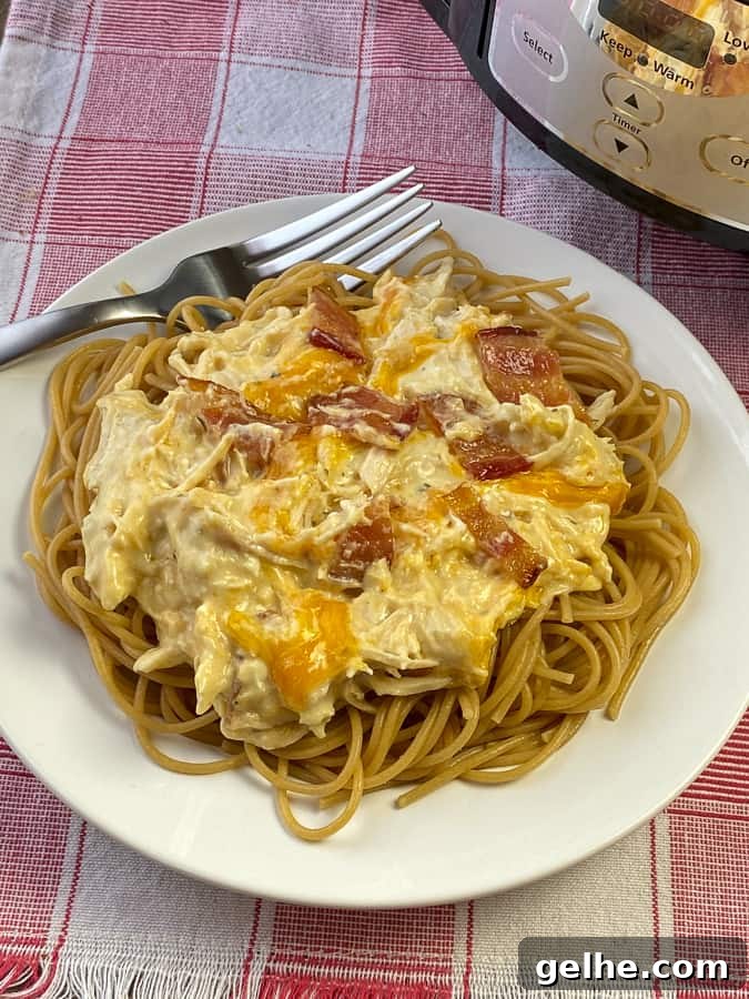 Crack chicken over spaghetti pasta on white plate with fork.