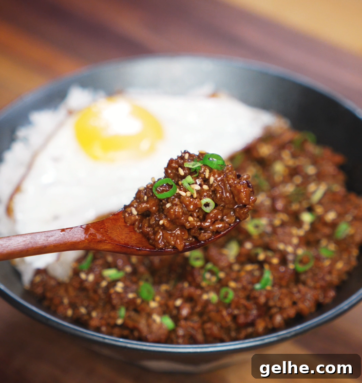 Wooden spoon lifting a flavorful bite of honey garlic beef over the rice bowl. The saucy beef is rich and glossy, with egg and rice in the background.