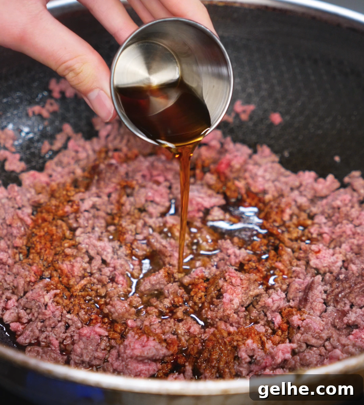 Pouring honey garlic sauce into a pan of browned ground beef. The sweet and savory glaze begins to sizzle and coat the meat as it cooks down.