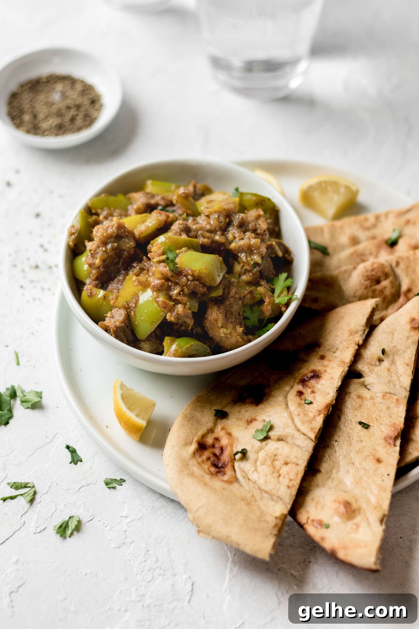 Instant Pot Goat Curry Close up of a bowl of Instant Pot Goat and Bell Pepper Curry on top of a white plate with naan and lemon wedges.