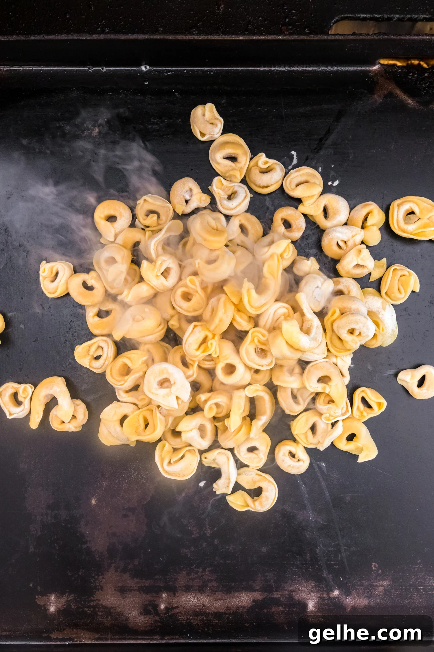 Cheese tortellini cooking on a hot flat-top griddle with steam rising.