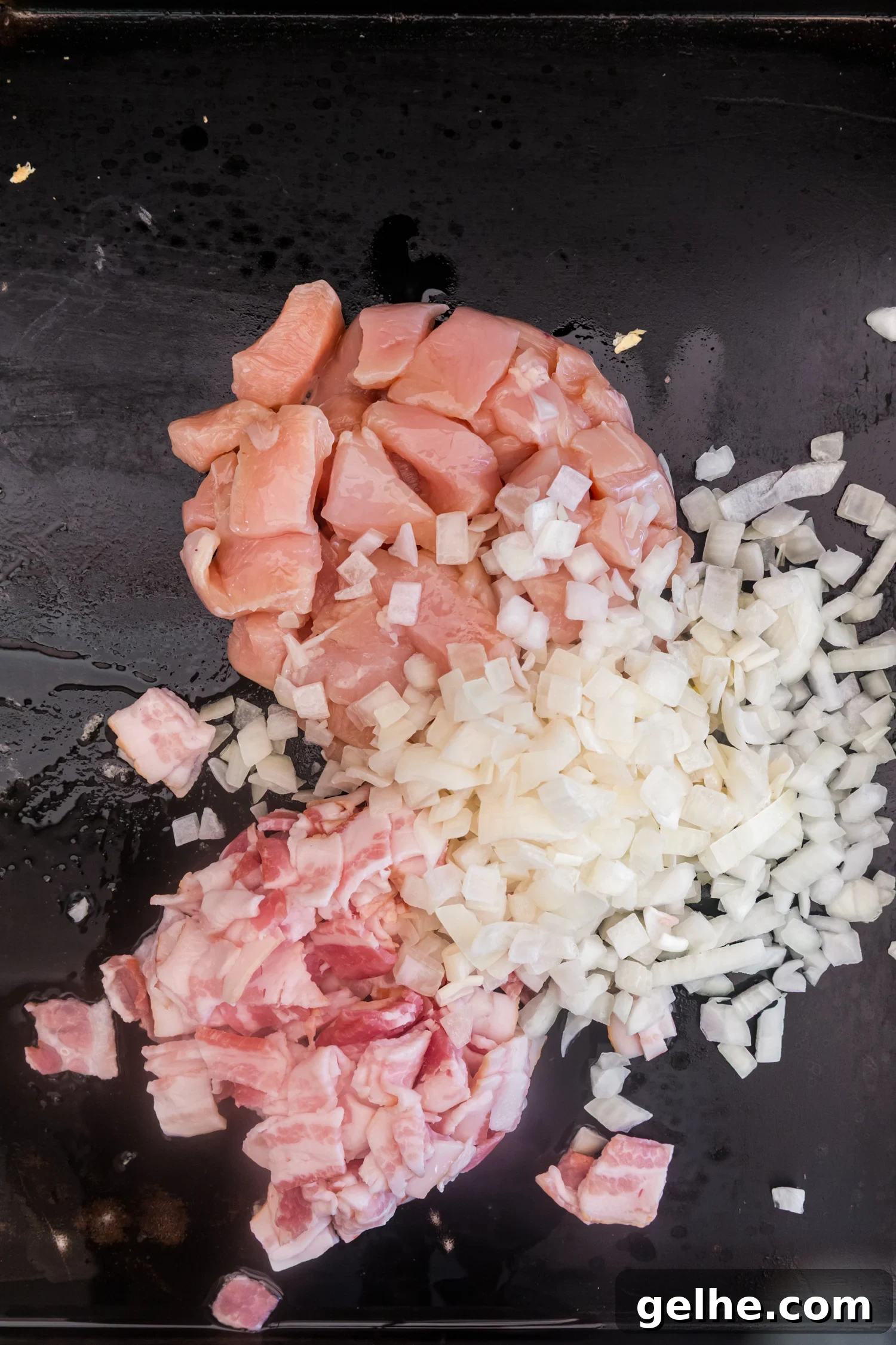 Diced chicken, chopped bacon, and diced onions cooking together on a flat-top griddle.