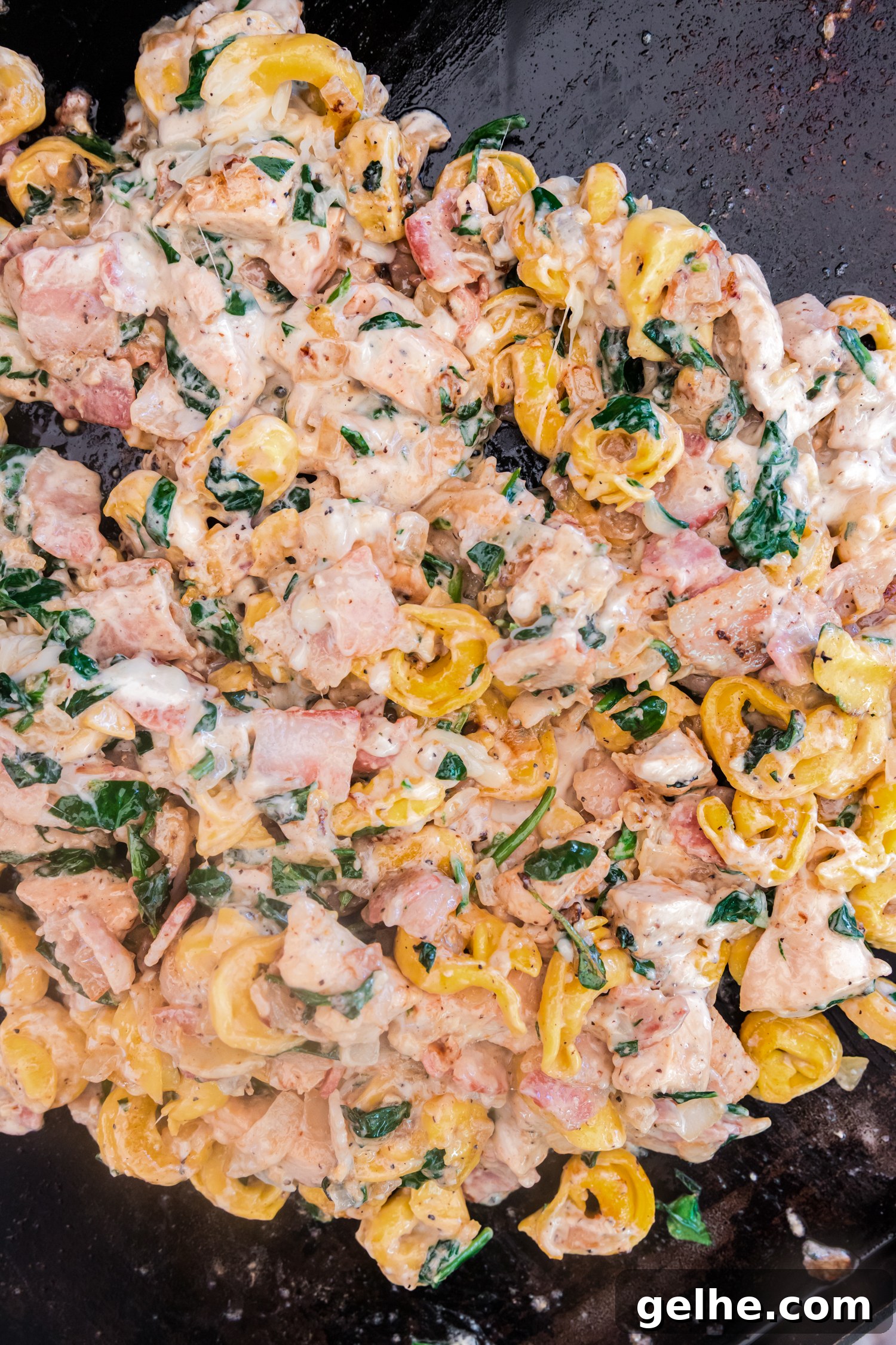 Chicken bacon ranch tortellini mixture cooking on a griddle with melted creamy sauce and spinach.