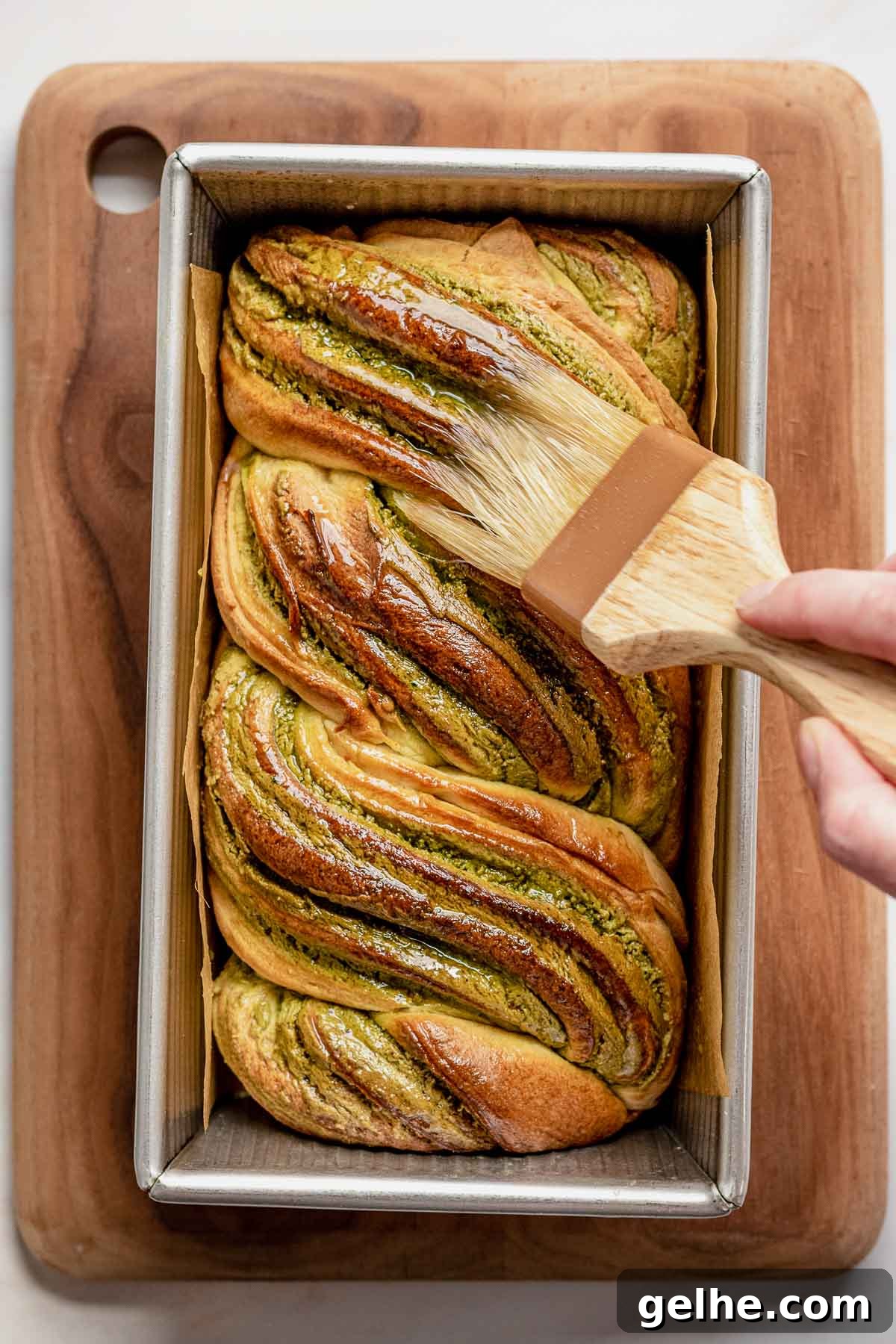 A hand brushes on simple syrup on the baked babka.